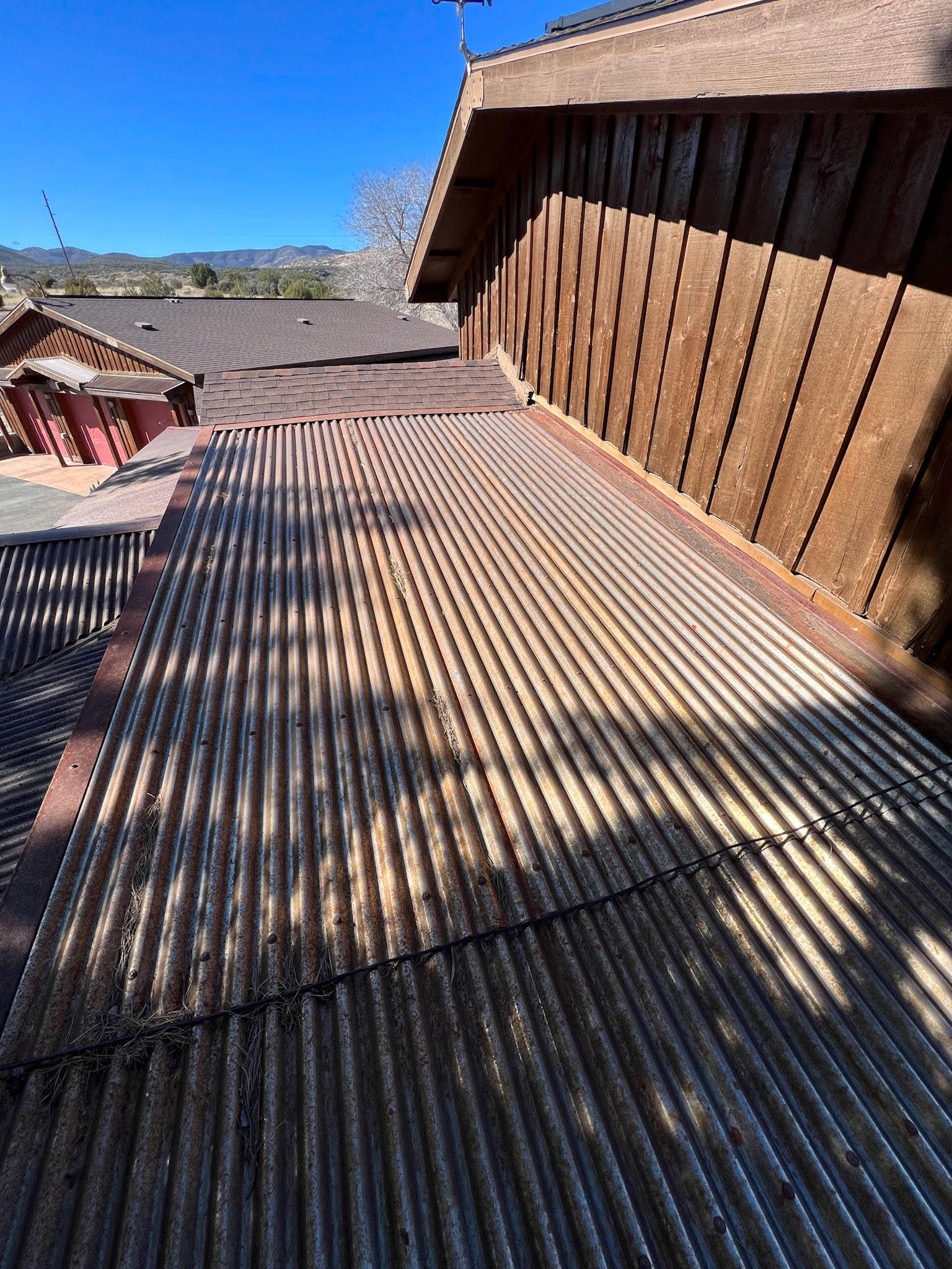 Corrugated metal roof on a building's side with vertical brown siding, bright blue sky.