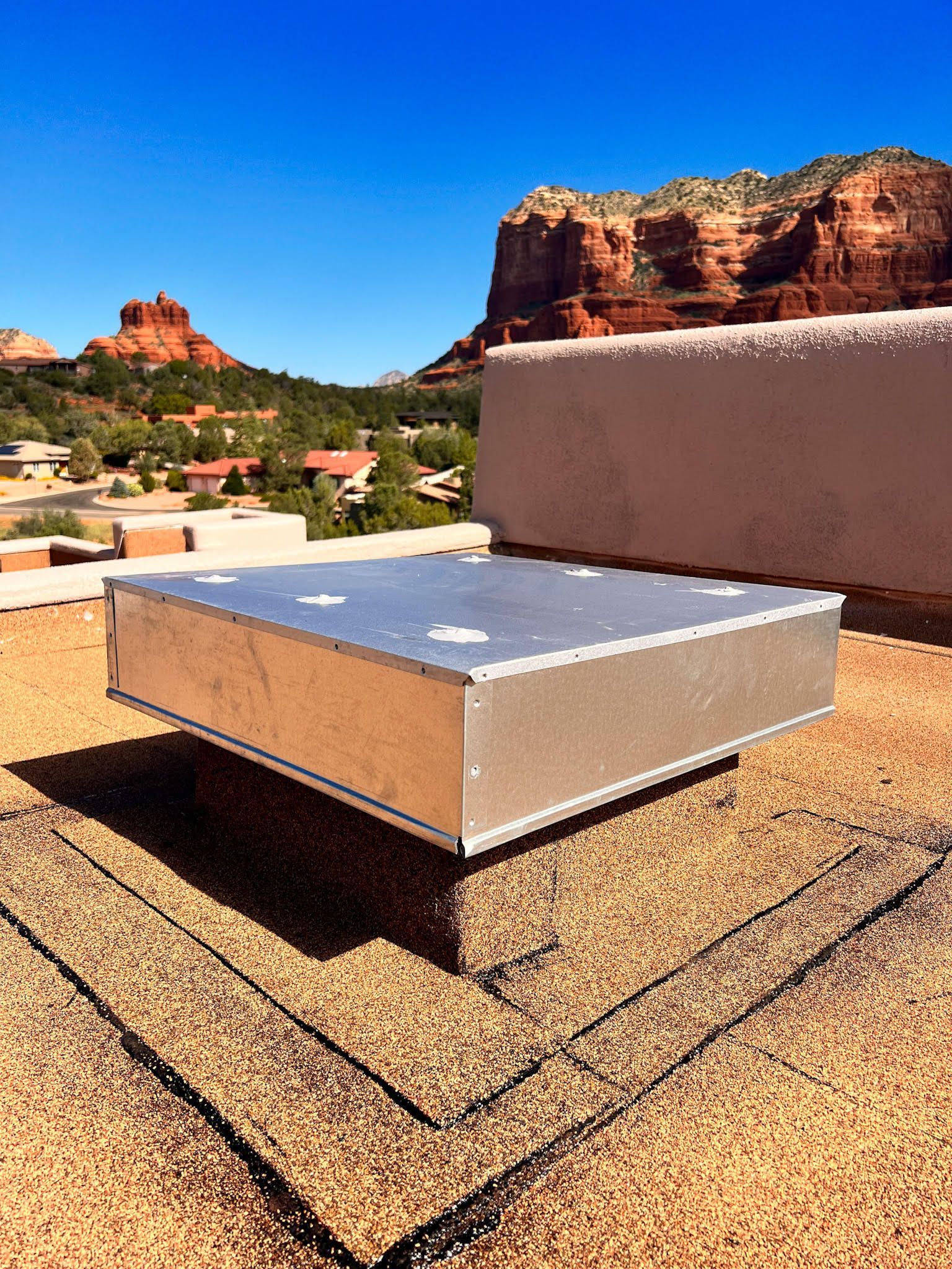 Silver HVAC unit on a rooftop with red rock formations in the background, sunny day.