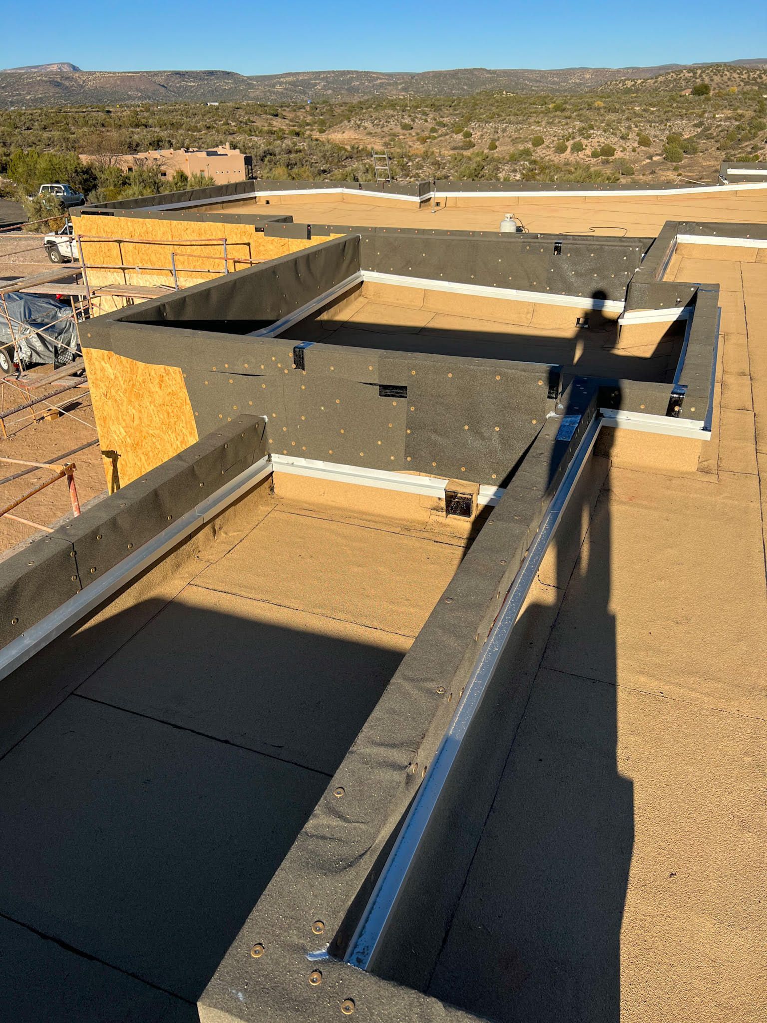 Construction site: Partially finished roof with black waterproofing and wooden borders, clear sky and distant hills.