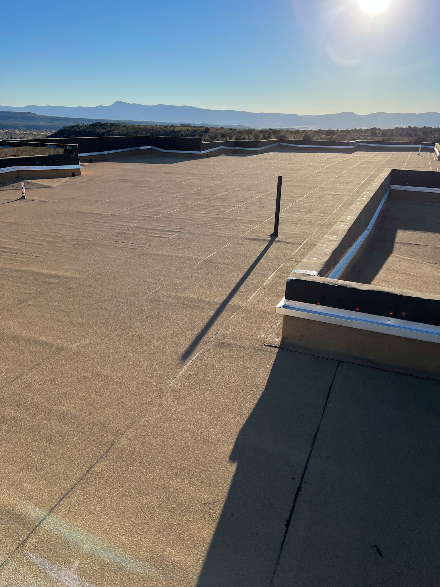 Flat roof with a pipe casting a long shadow in the sun, distant mountains in view.