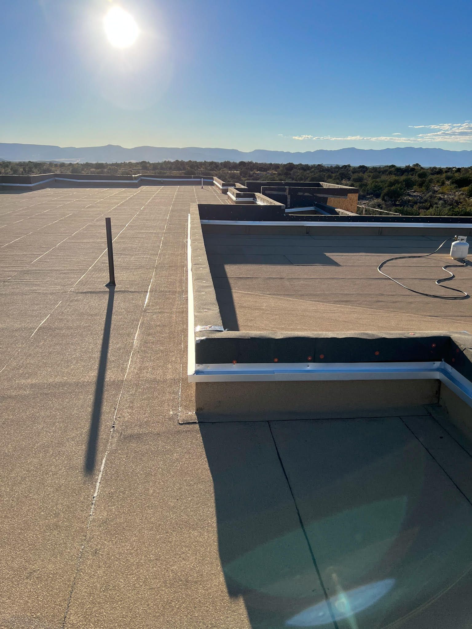 Flat rooftop with sun, clear sky, and distant mountains.