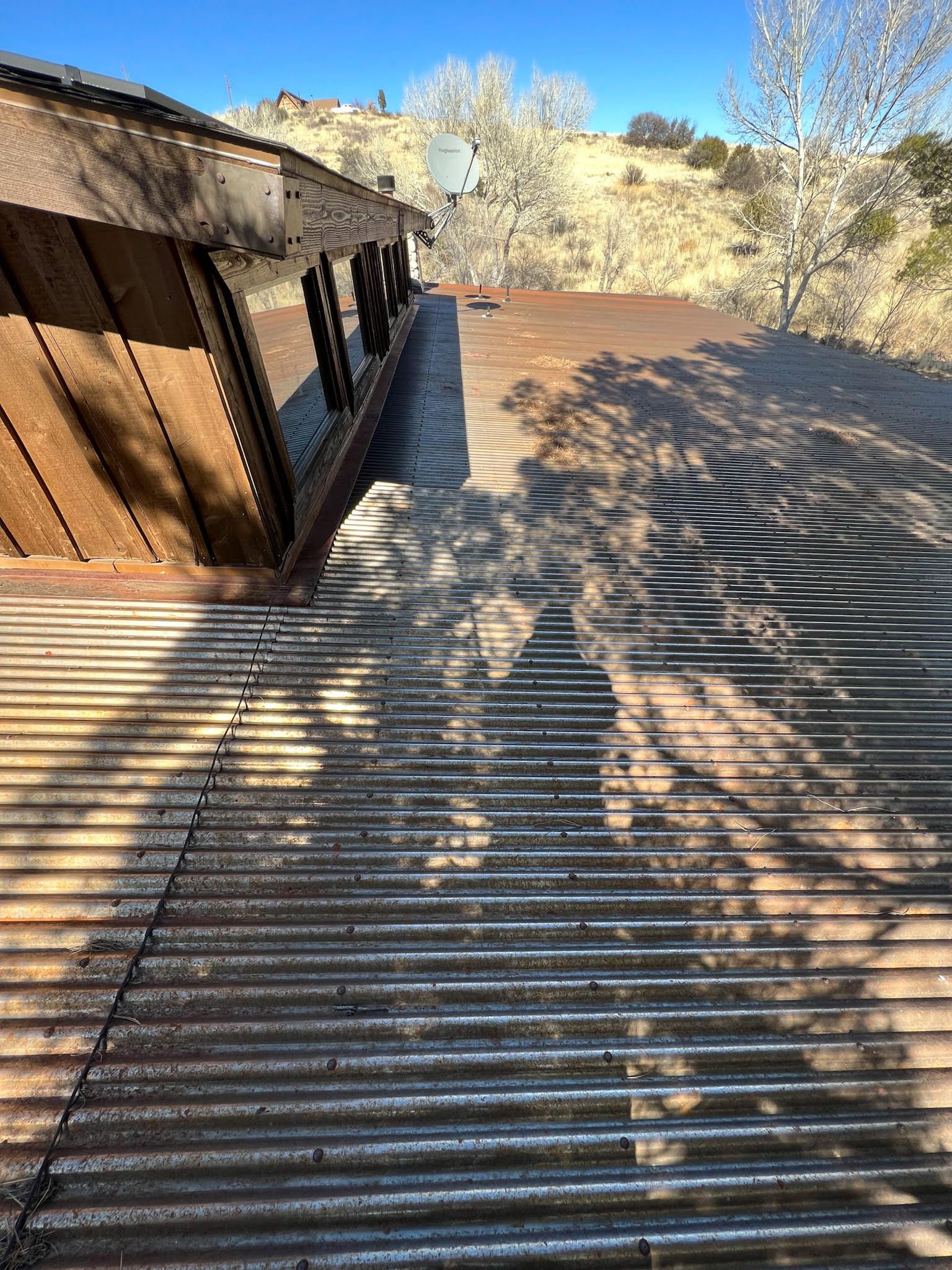 Corrugated metal roof of a building, with wood siding on the left and a satellite dish in the background.
