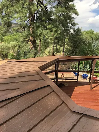 Brown wooden deck with railing and roof, overlooking a forest.