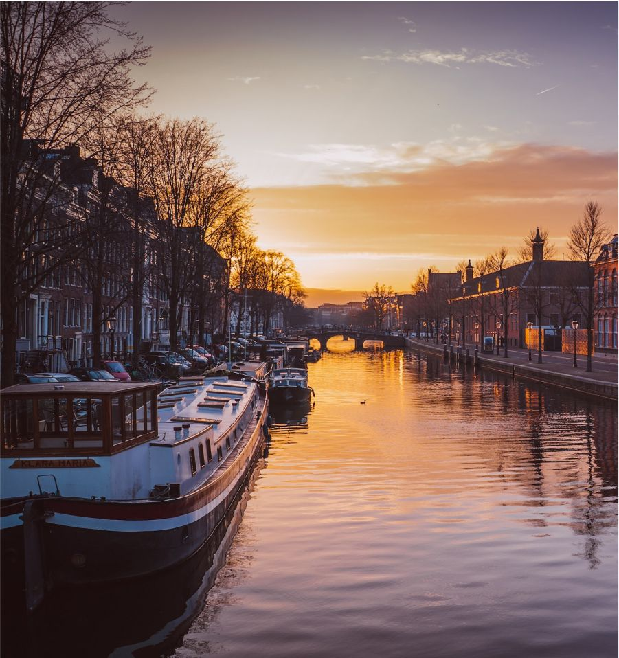 阿姆斯特丹的運河在日落時分,船屋、橋樑和建築物倒映在金色的陽光下。