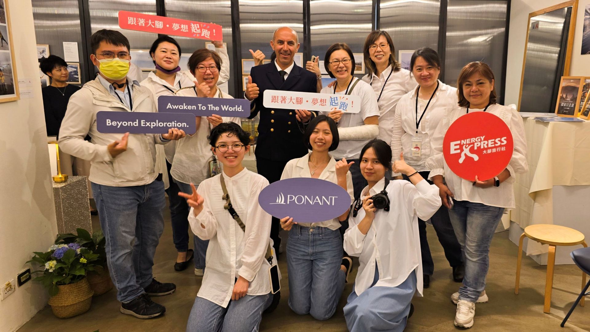 一群人手持標語，在室內擺姿勢拍照。有些人面帶微笑，其中一人身穿制服。