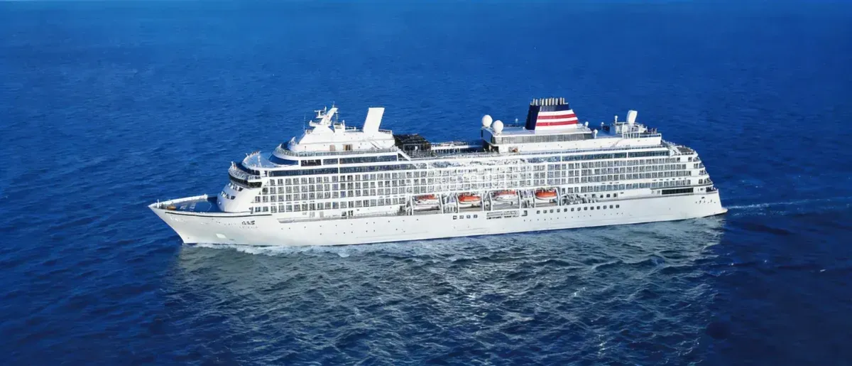 A large white cruise ship sails on the blue ocean.