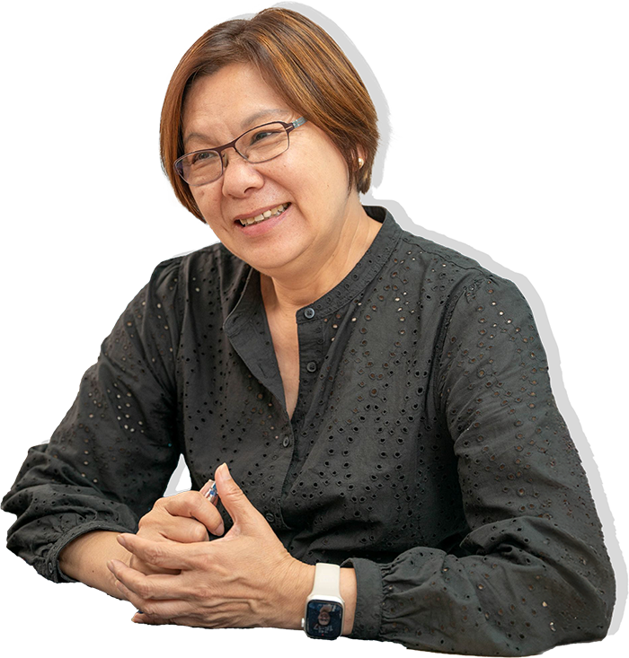 一位戴眼鏡的女士面帶微笑，身穿深灰色紐帶襯衫，留著棕色短髮，坐在桌前。