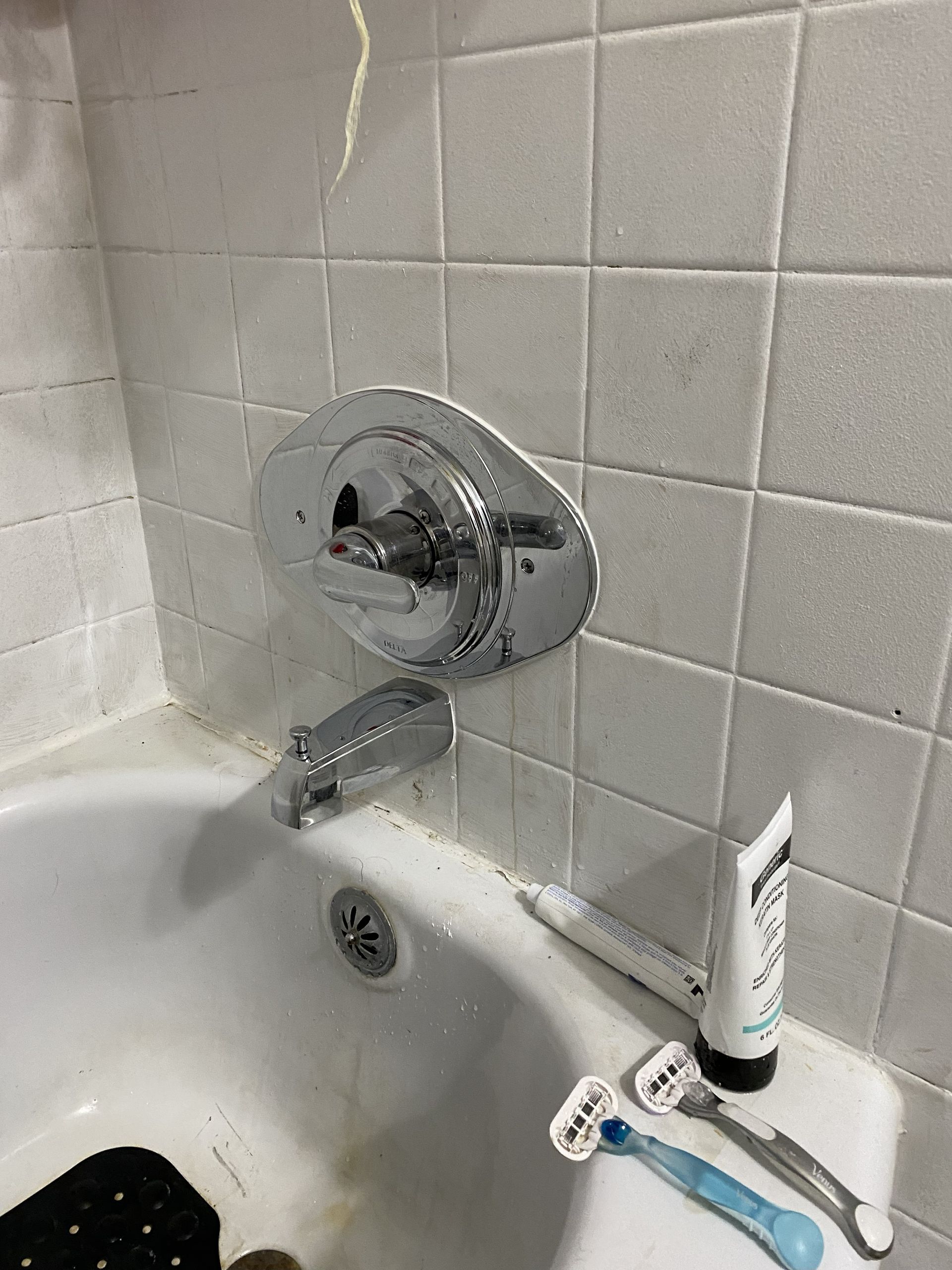 Bathtub with faucet and toiletries on the edge, white tiles in background.