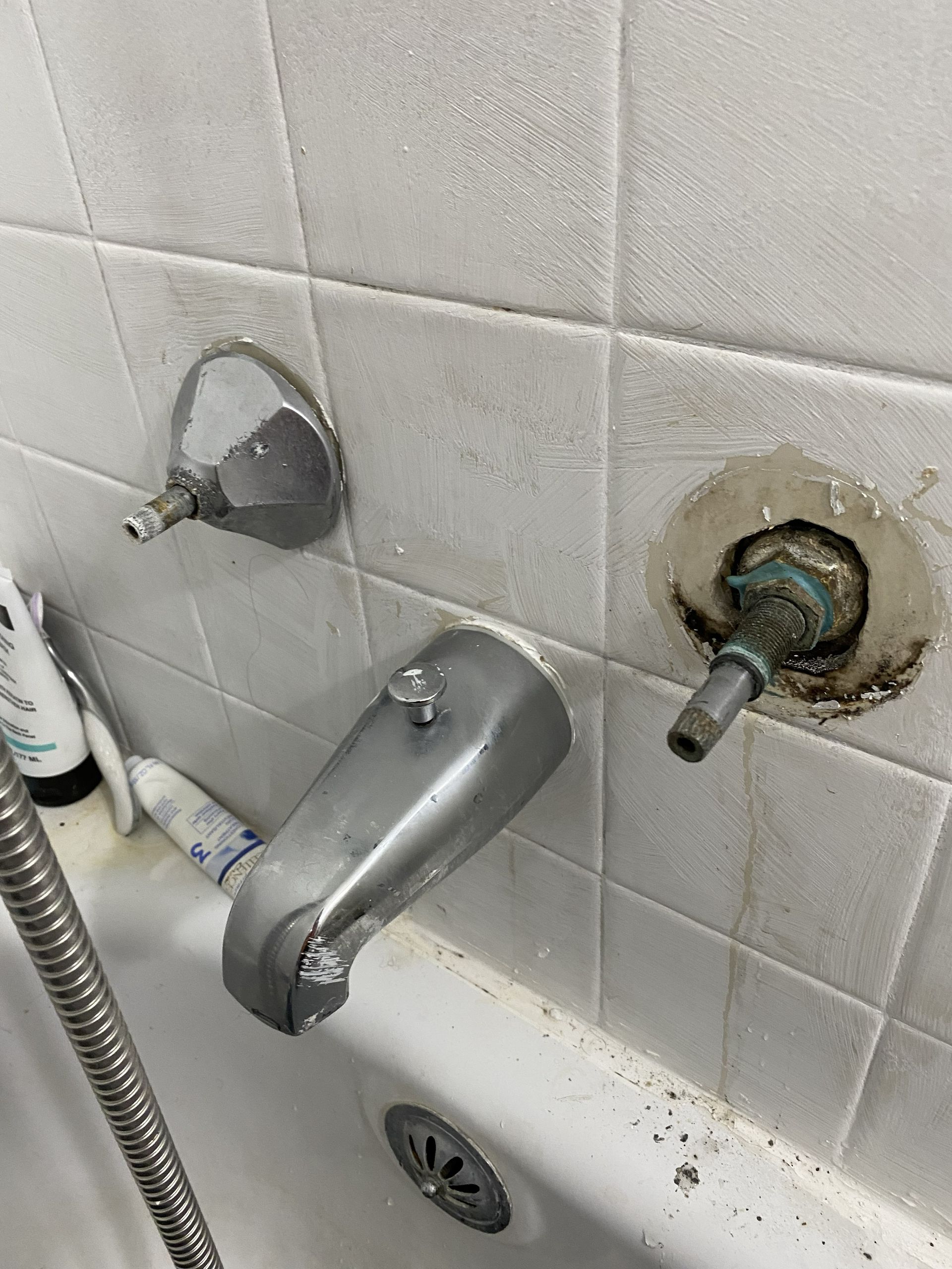 Shower with damaged faucet and surrounding stained tiles; silver fixtures.