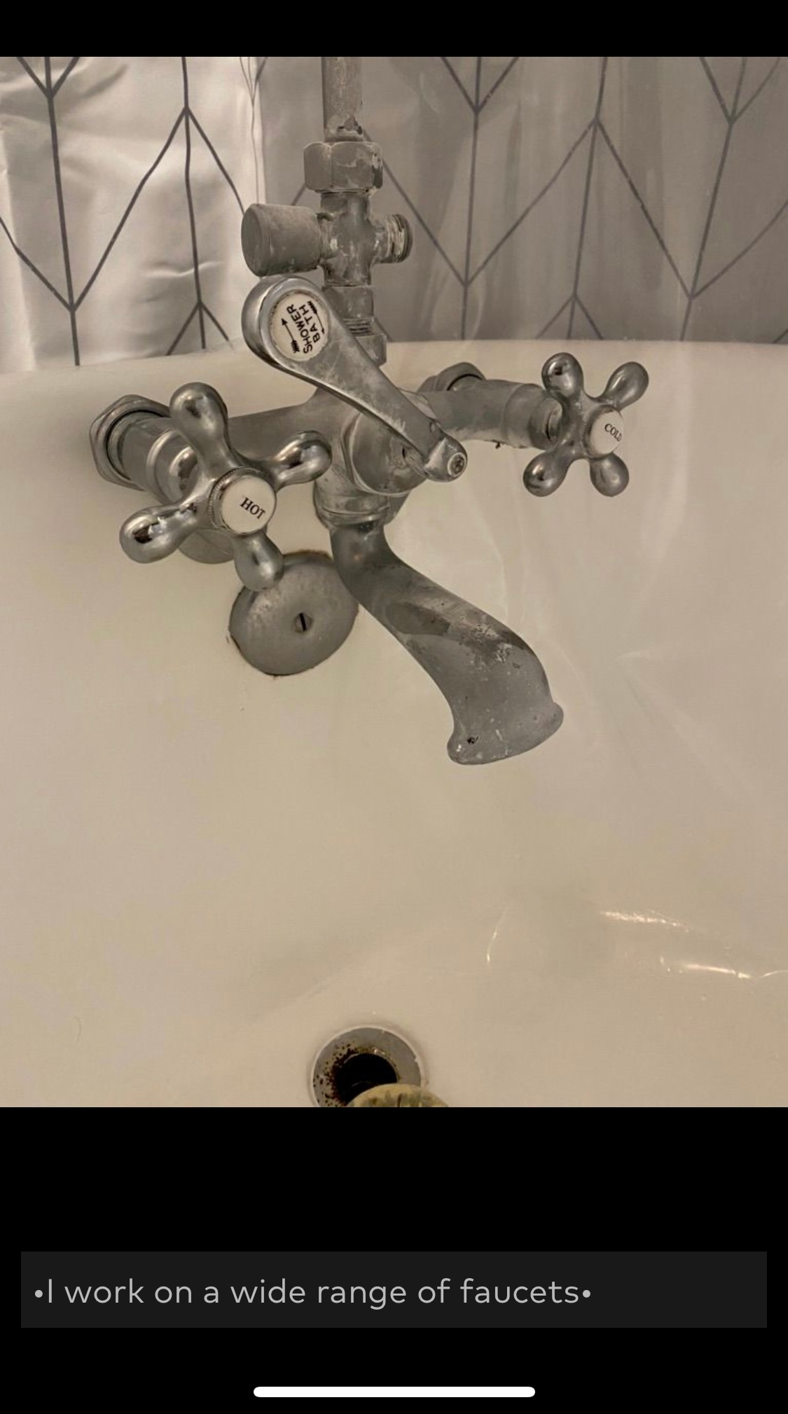 Antique chrome faucet set in a white bathtub; in front of a patterned shower curtain.