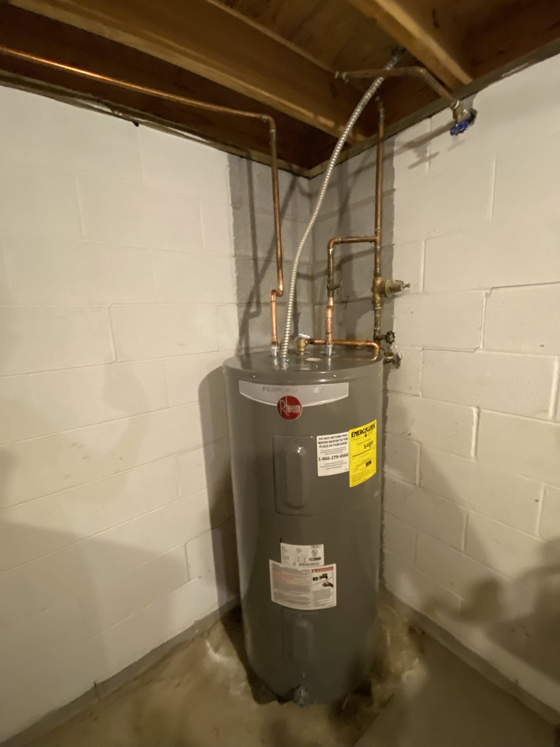 Water heater in a corner, with copper pipes and concrete walls.