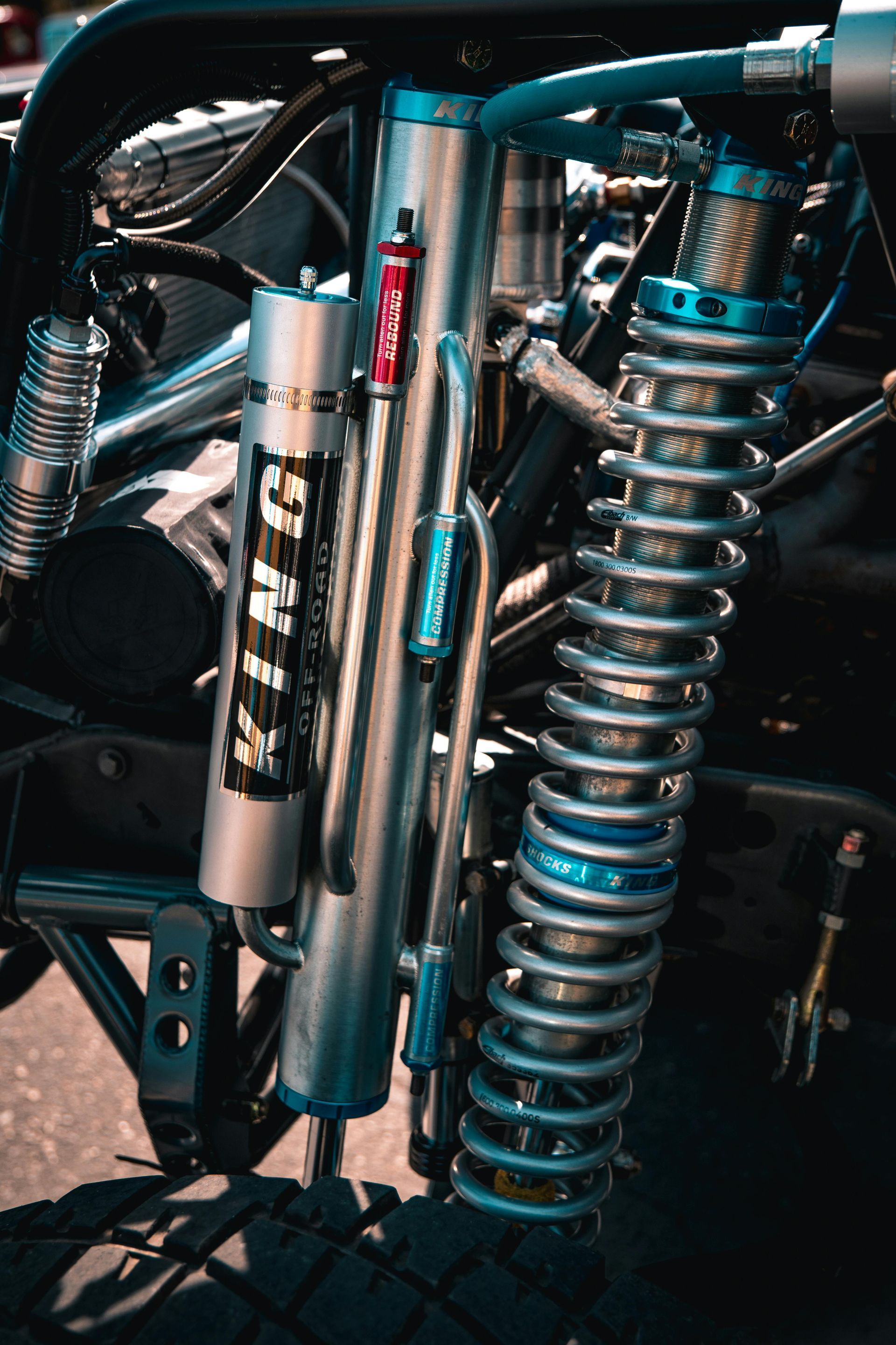 Close-up of a vehicle's suspension system with shocks, coil springs, and tubing in silver and blue tones.
