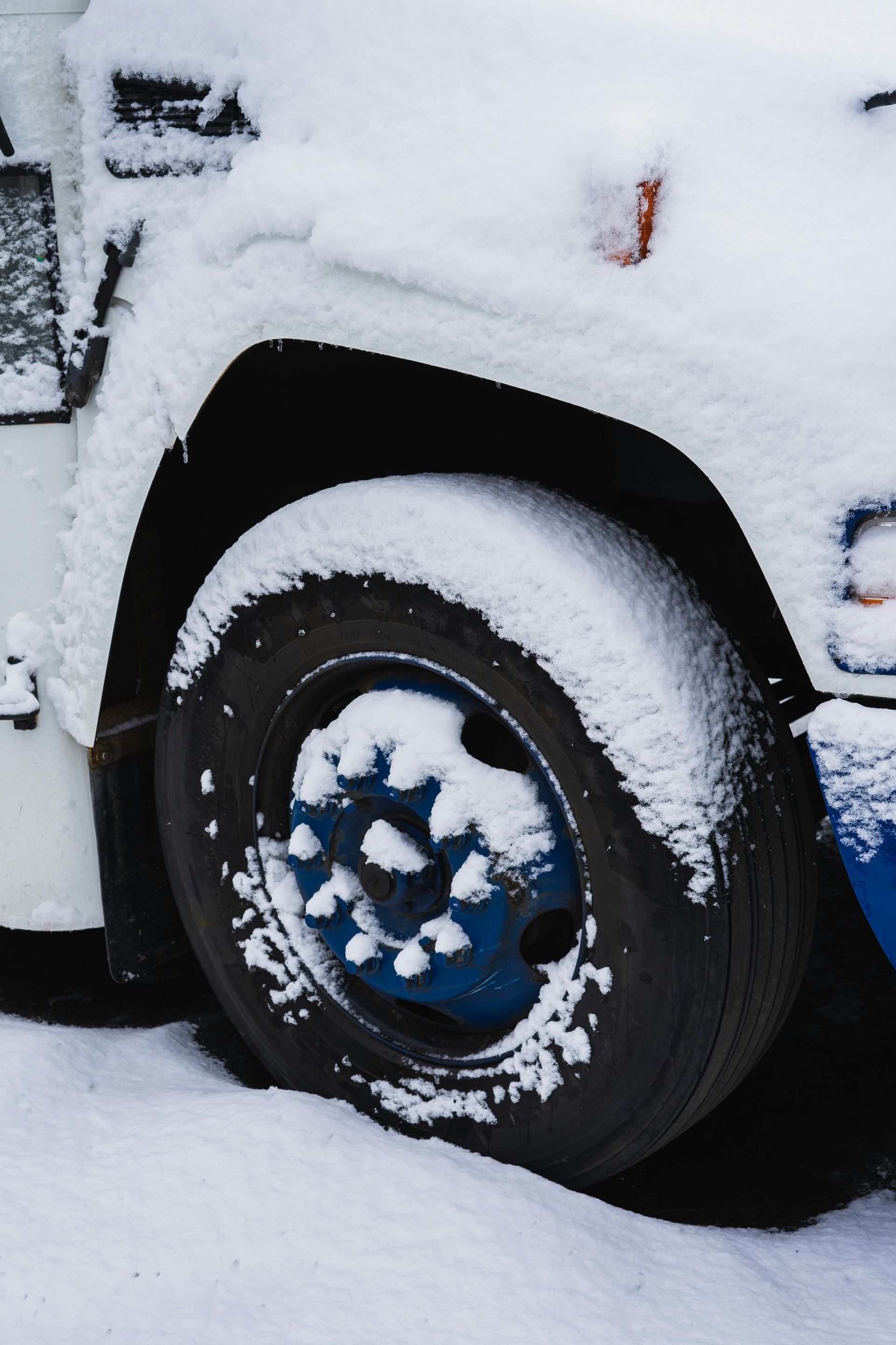 Snow-covered truck tire and wheel, with white snow on the vehicle.
