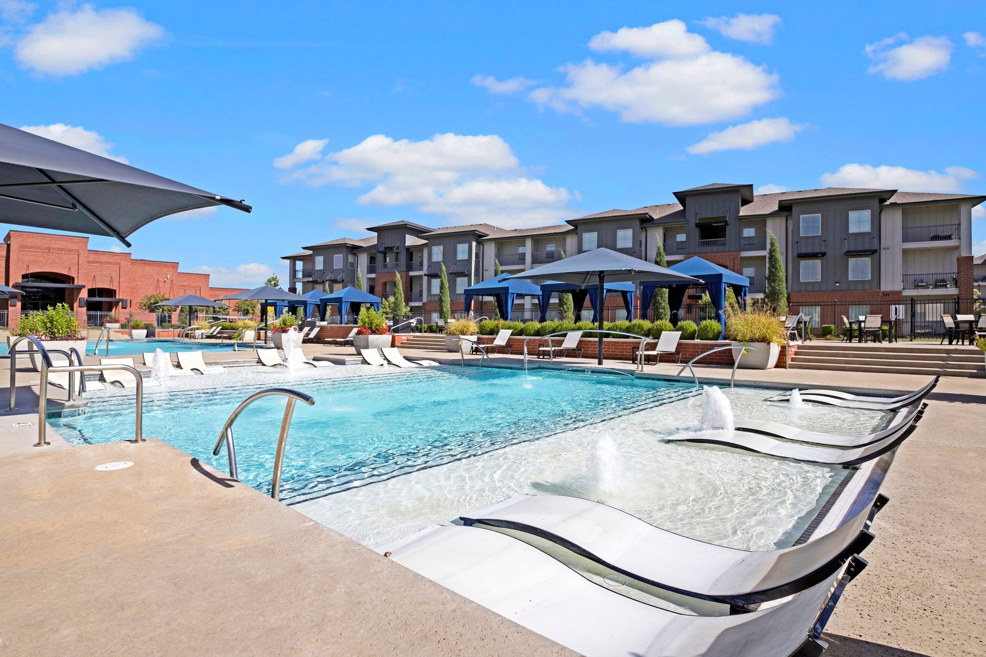 A large swimming pool with chairs and umbrellas in front of a building.