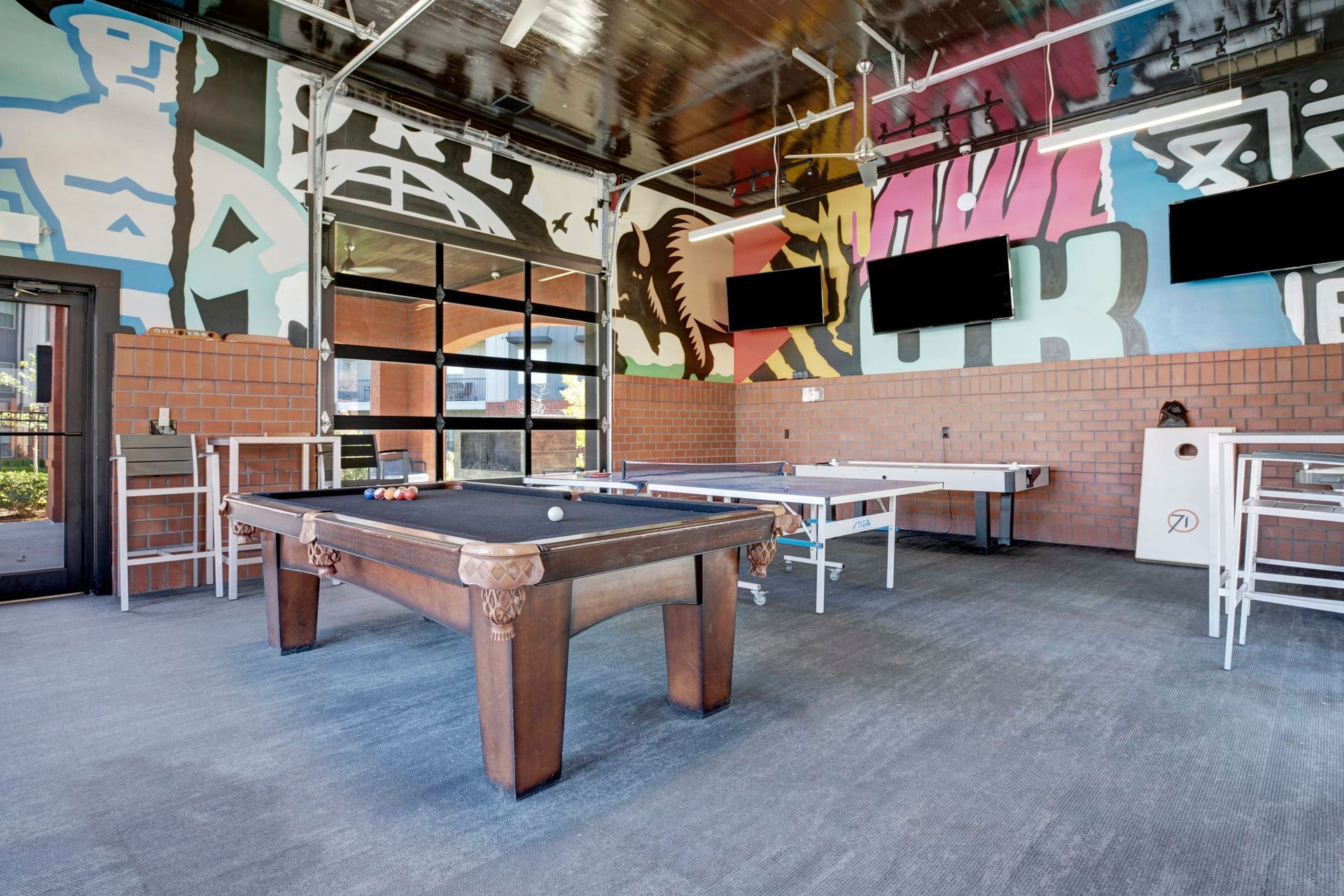 A pool table and ping pong tables in a room with graffiti on the walls.