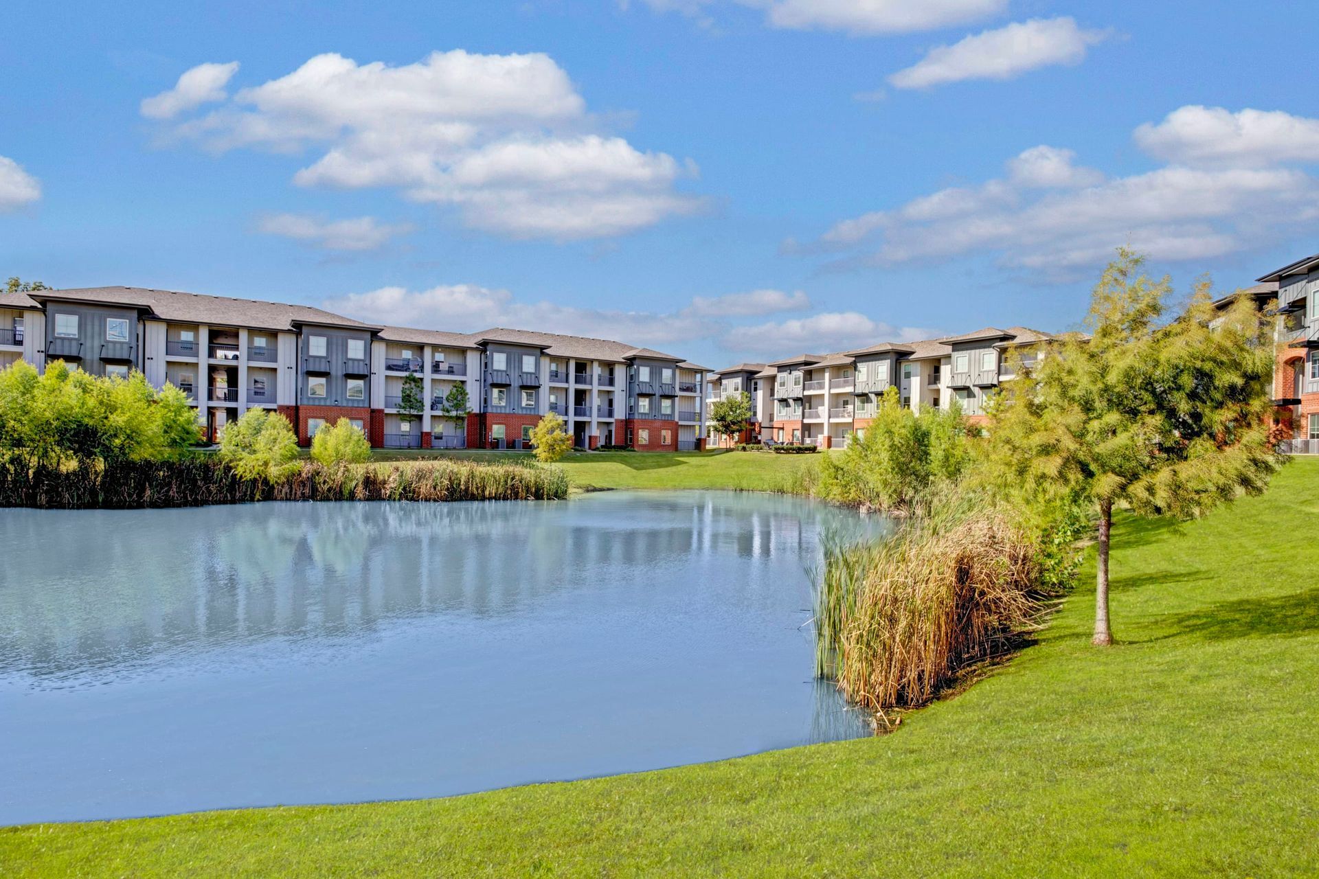 There is a lake in the middle of a grassy field in front of a building.