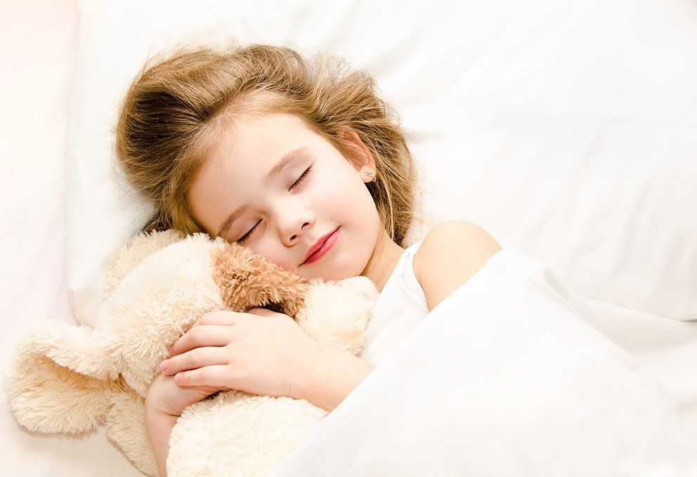 Happy child snuggling in her bed with a teddy bear