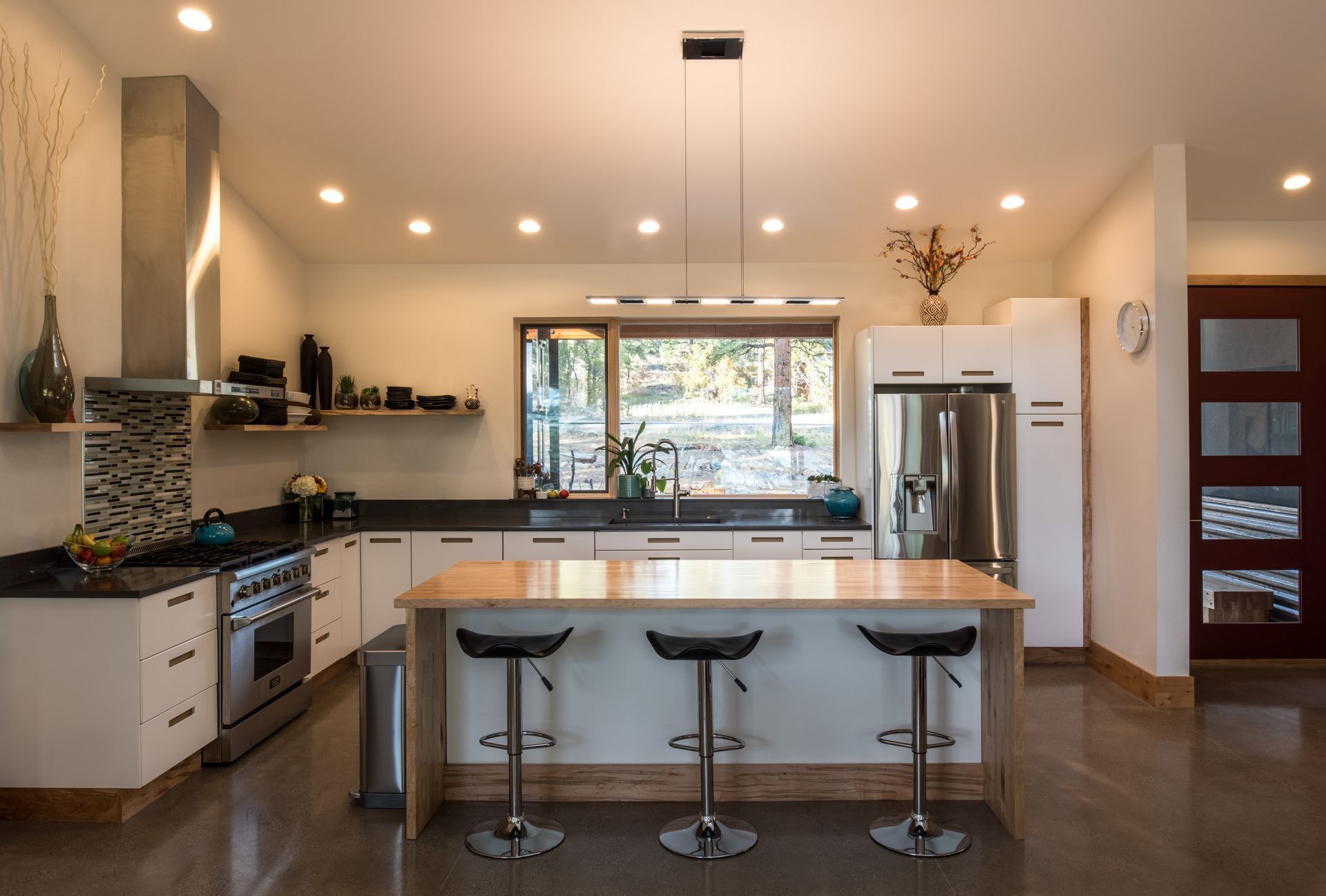 A kitchen with white cabinets , stainless steel appliances , a large island and stools.