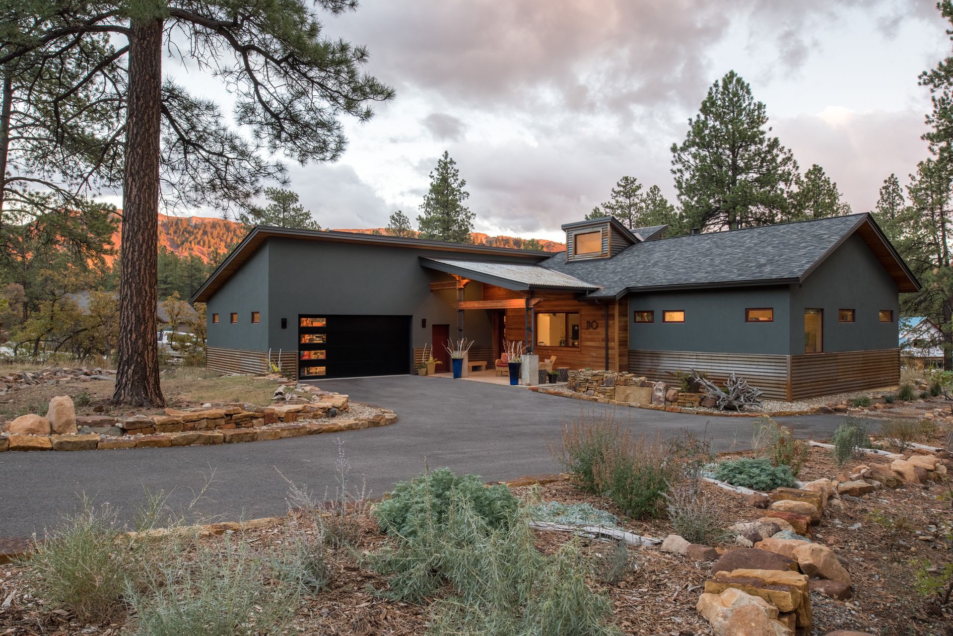 A large house with a garage is surrounded by trees and rocks.