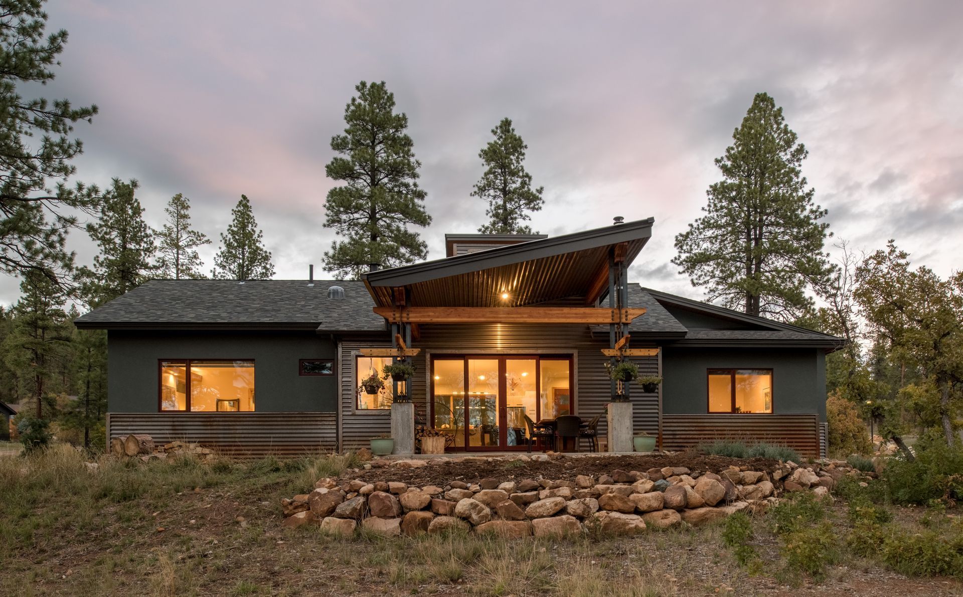 The back of a house with a lot of windows is surrounded by trees.