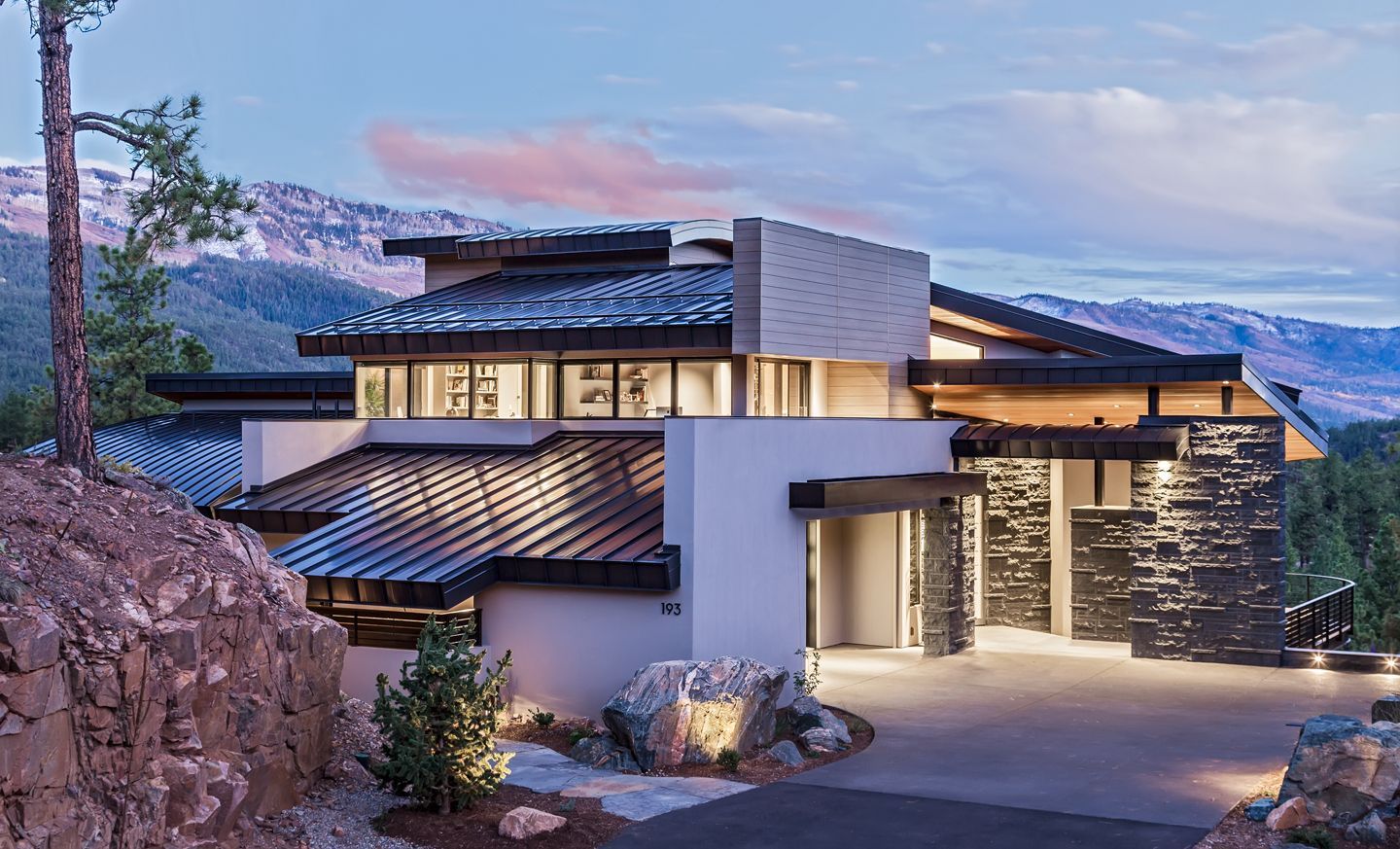 A modern house is sitting on top of a hill with mountains in the background.