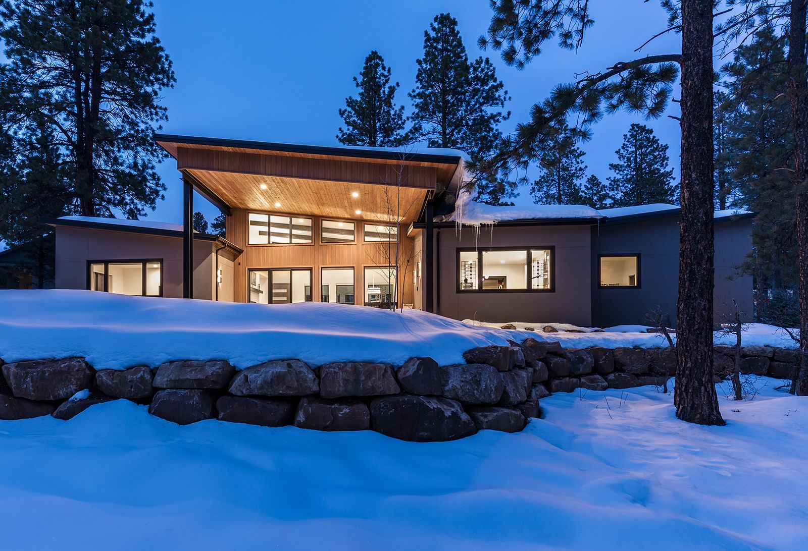 A house is sitting on top of a snow covered hill surrounded by trees.