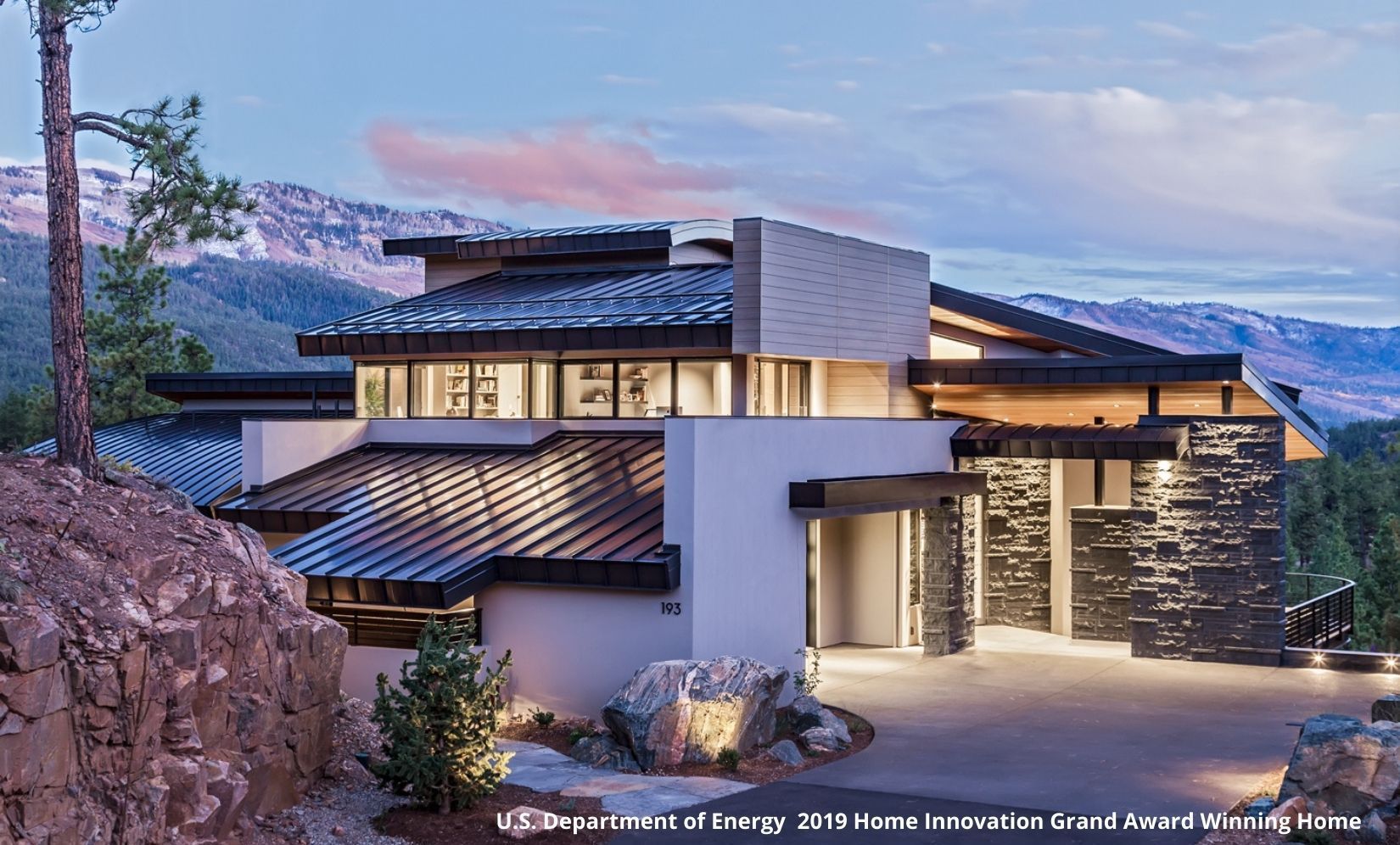 A large house is sitting on top of a hill with mountains in the background.