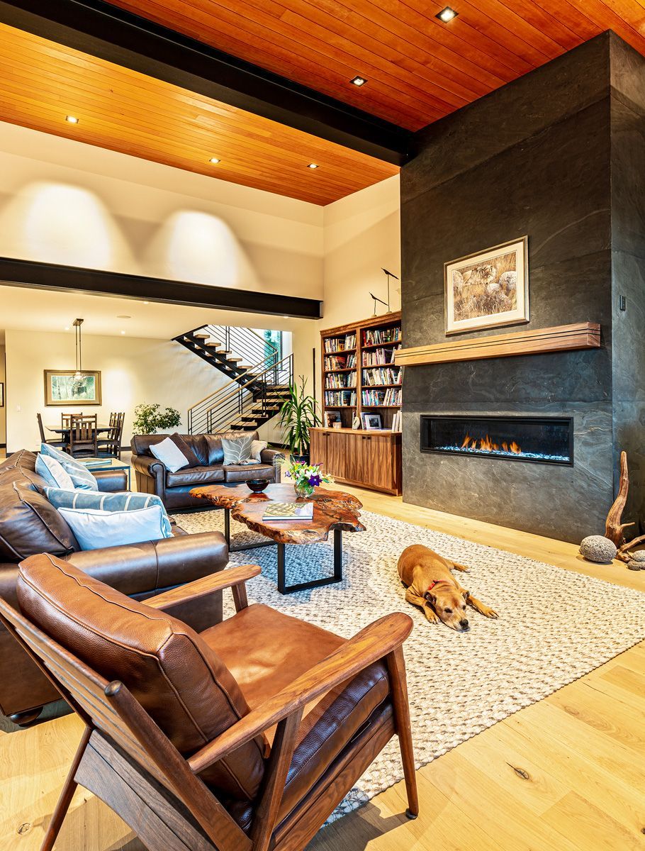 A living room with a fireplace , chairs , a couch and a dog.