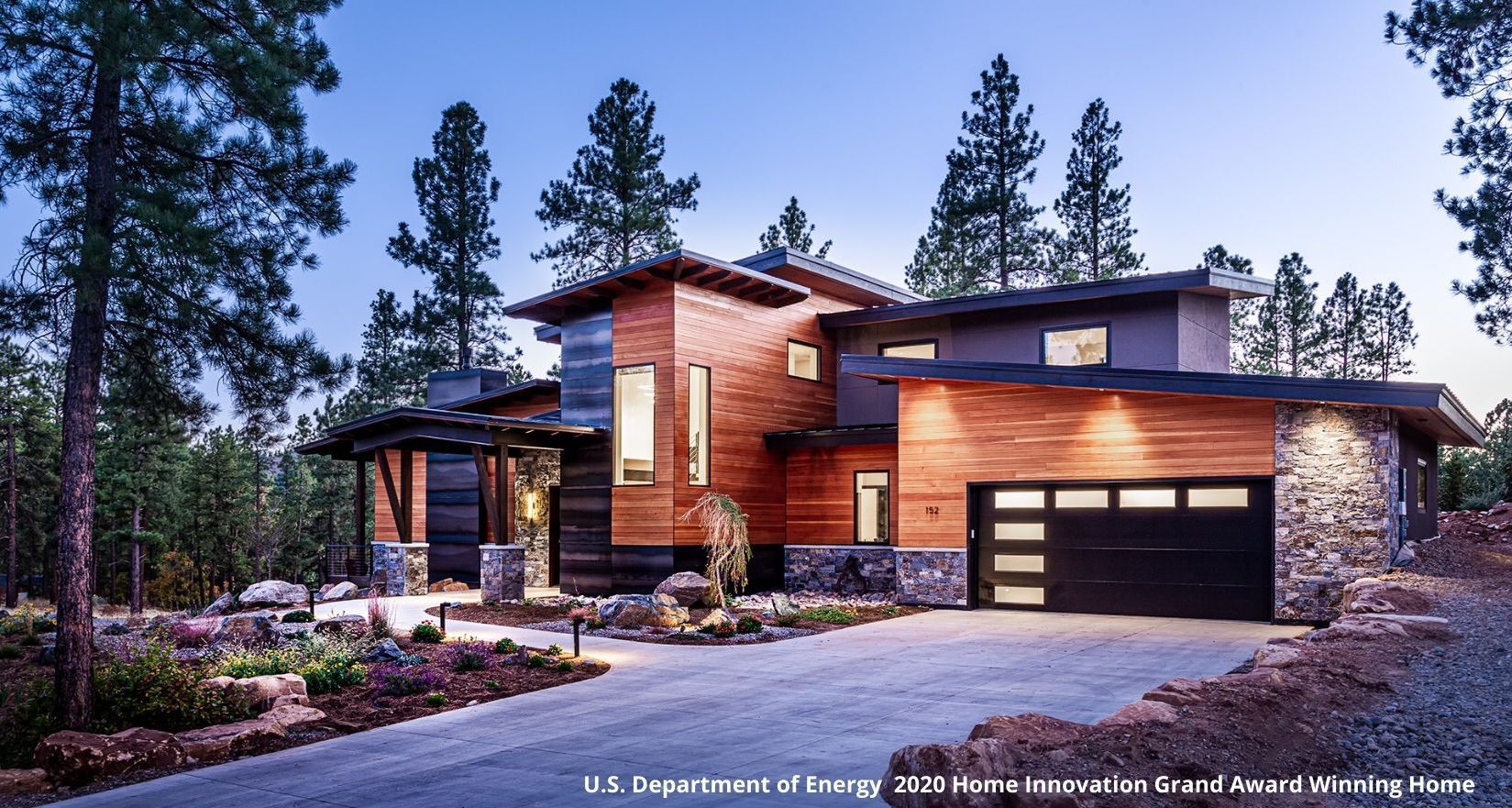 A house with a black garage door is surrounded by trees