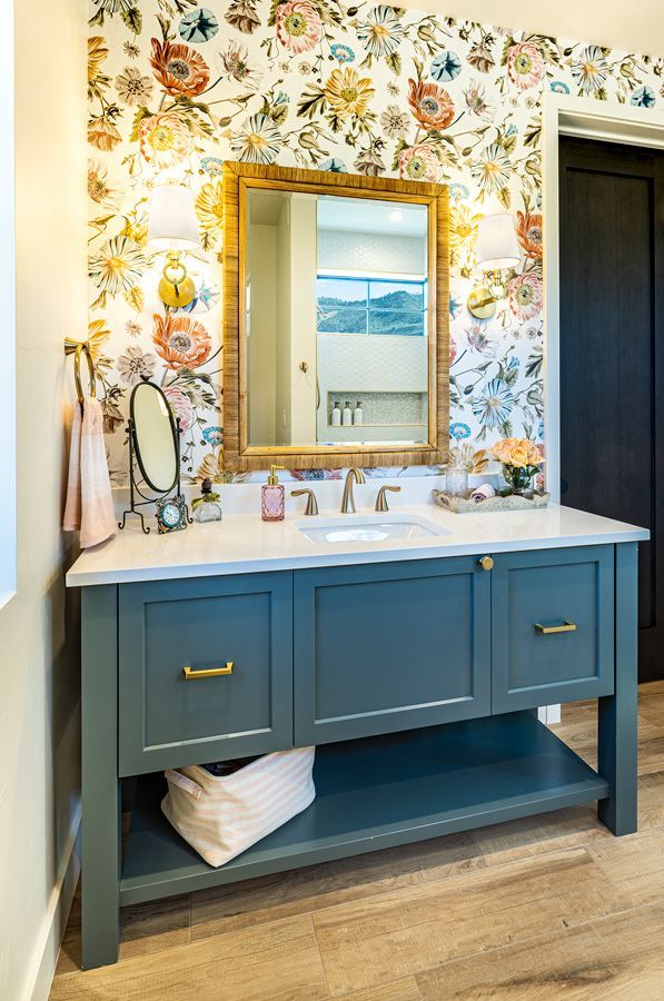 A bathroom with a sink , mirror , and floral wallpaper.
