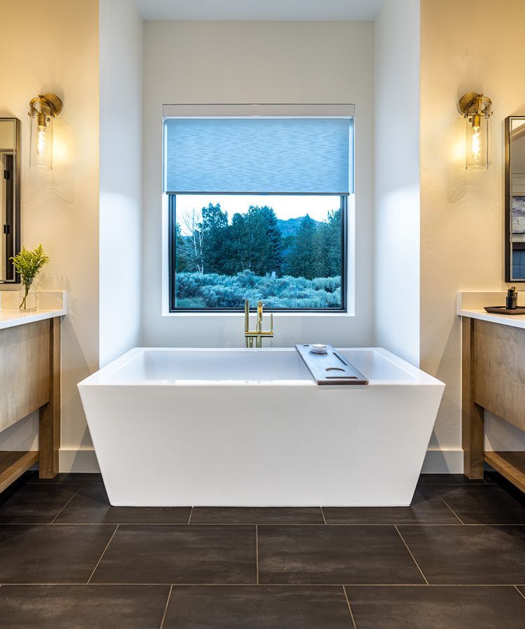 A bathroom with two sinks and a bathtub in front of a window.