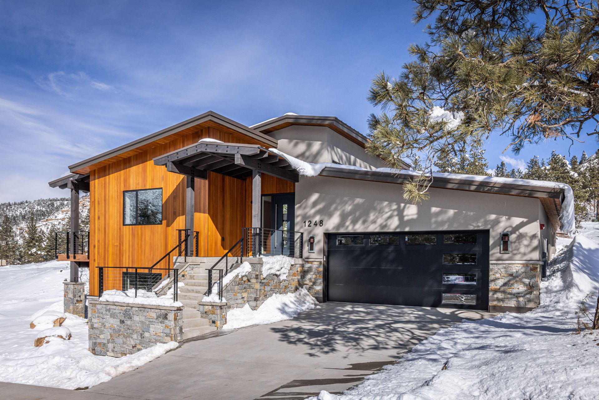 A house with a garage is sitting on top of a snow covered hill.