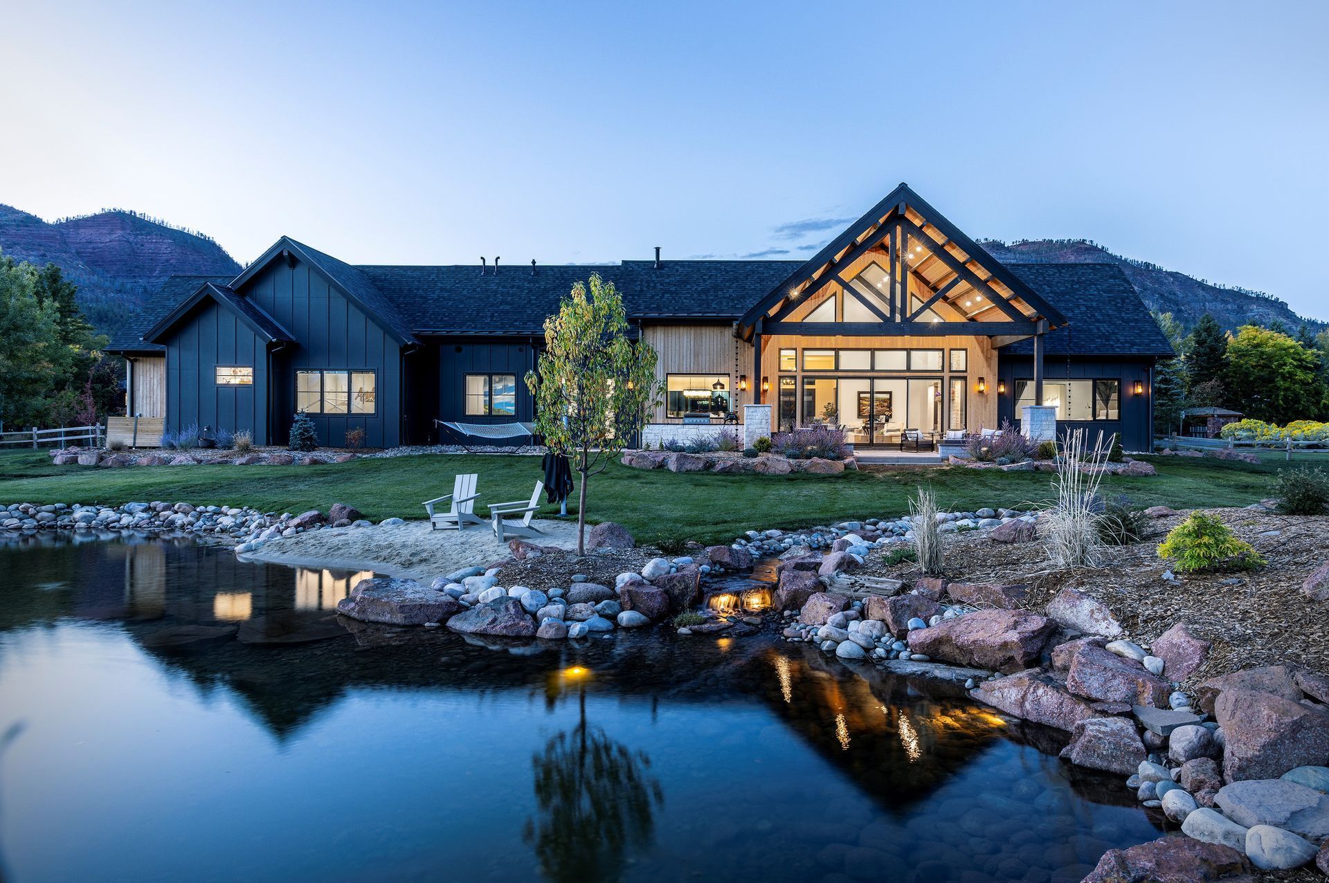 A large house with a pond in front of it and mountains in the background.