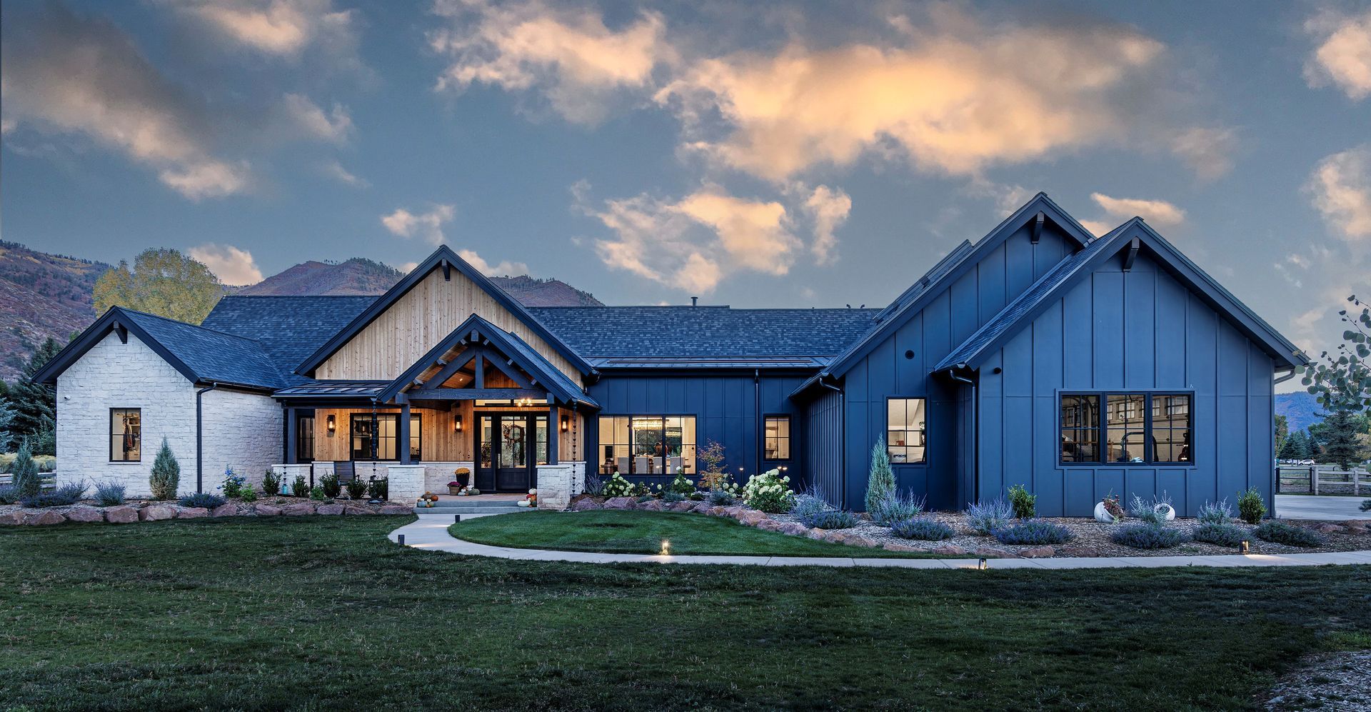 A large blue and white house with a blue roof is sitting on top of a lush green field.