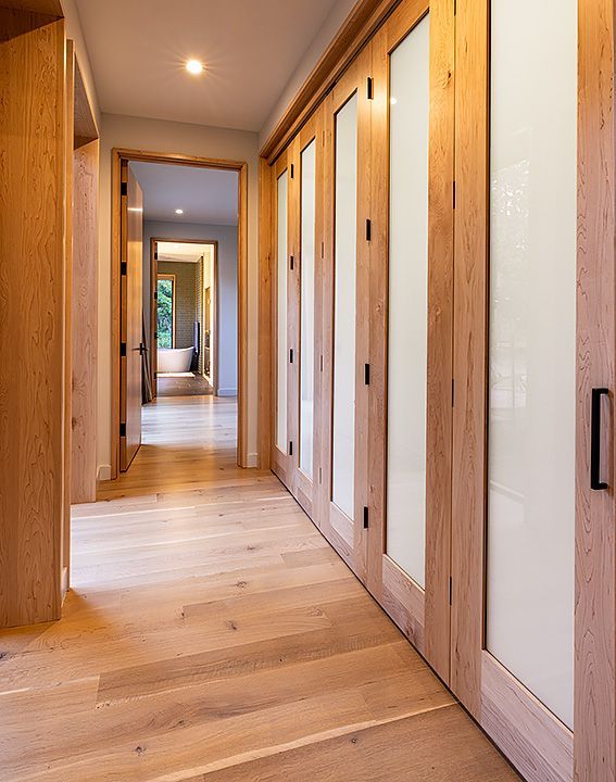A hallway with wooden floors and glass doors leading to a bathroom.