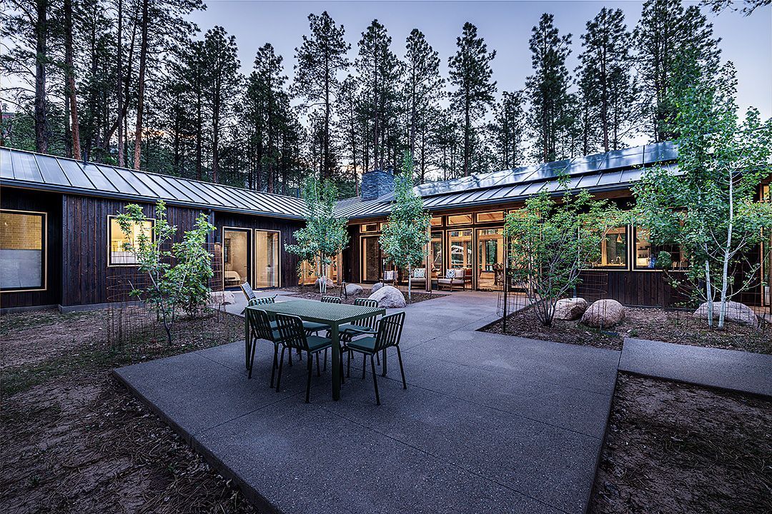 A patio with a table and chairs in front of a house in the middle of a forest.