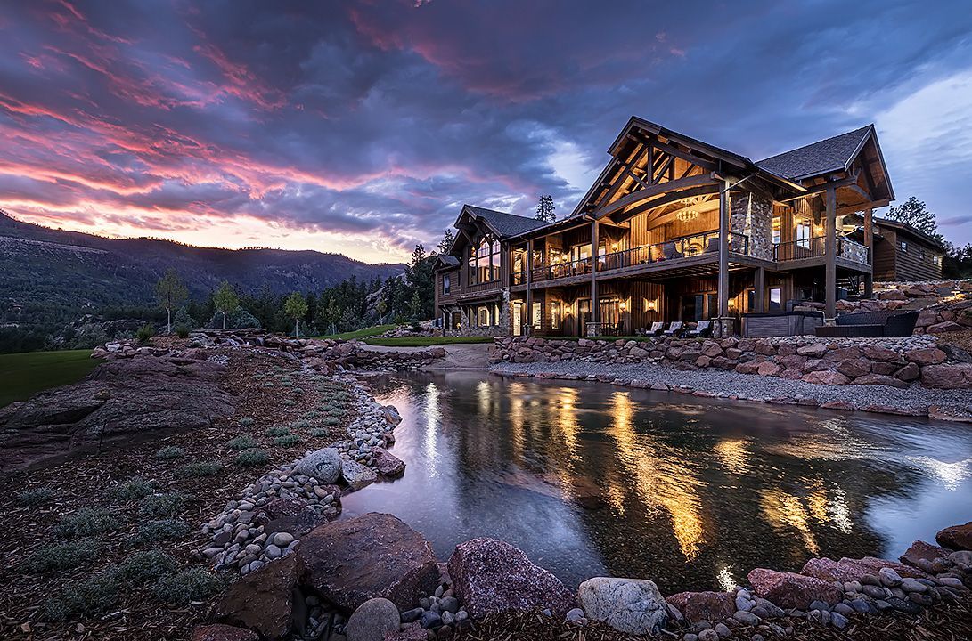 A large house is sitting on top of a hill with mountains in the background at sunset.