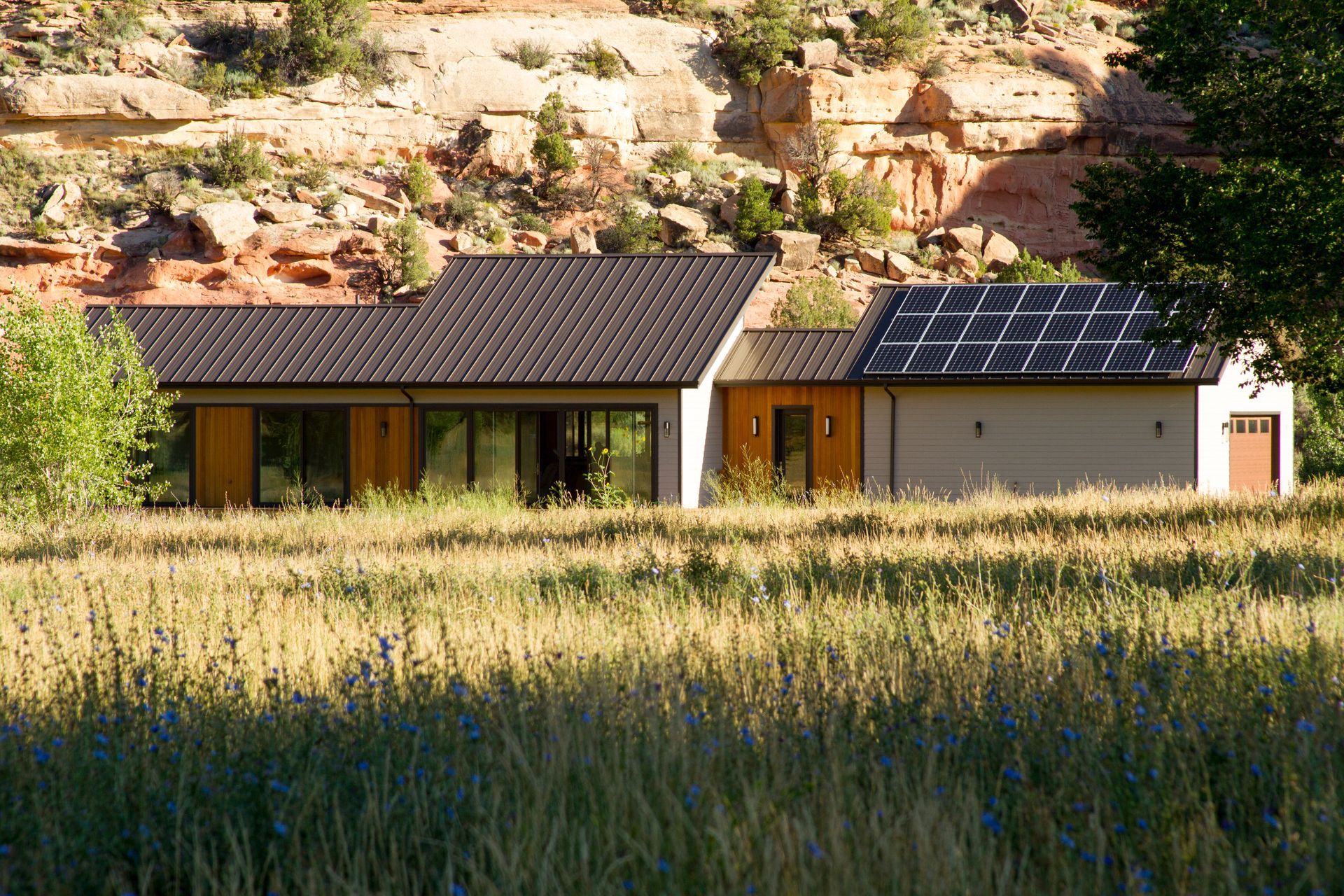 A house with solar panels on the roof is sitting in the middle of a grassy field.