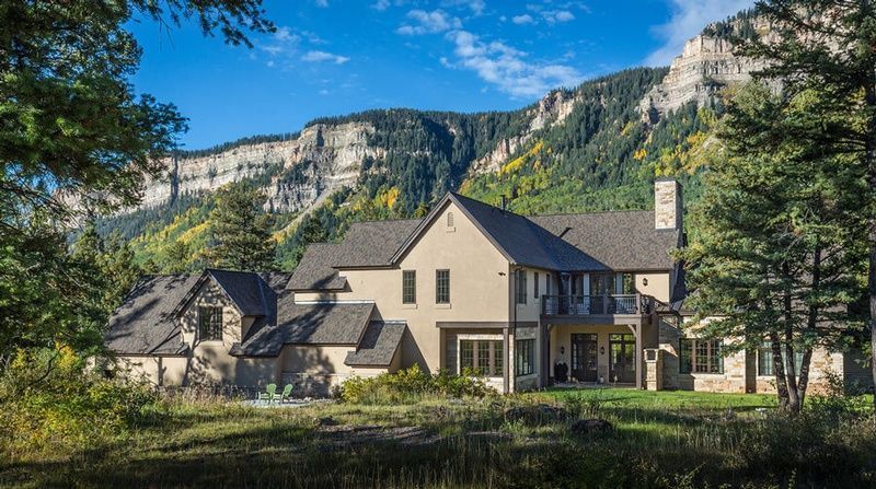 A large house is sitting in the middle of a field with mountains in the background.