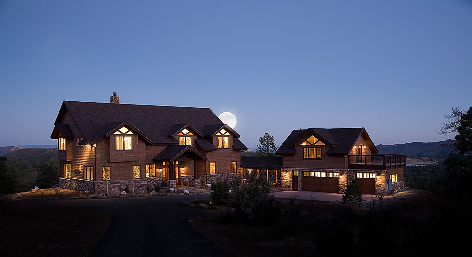 A large house is lit up at night with a full moon in the background