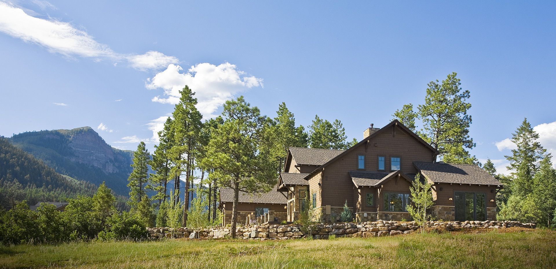 A large house in the middle of a field with mountains in the background