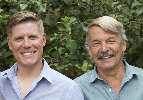 Two men are smiling for a picture in front of a tree.