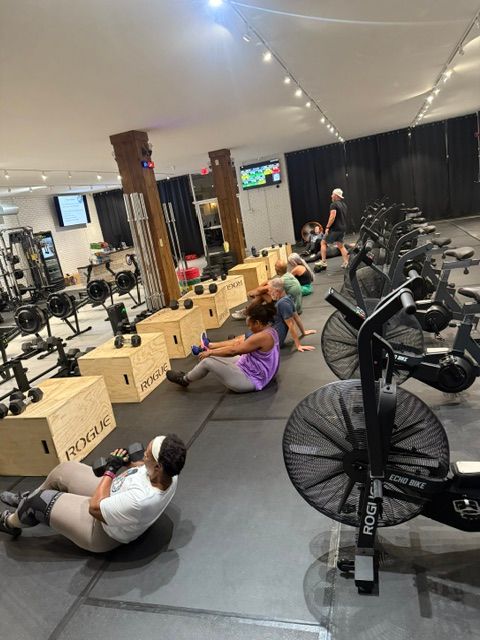 People exercising in a gym; some sit-ups, others on fan bikes and with weights.