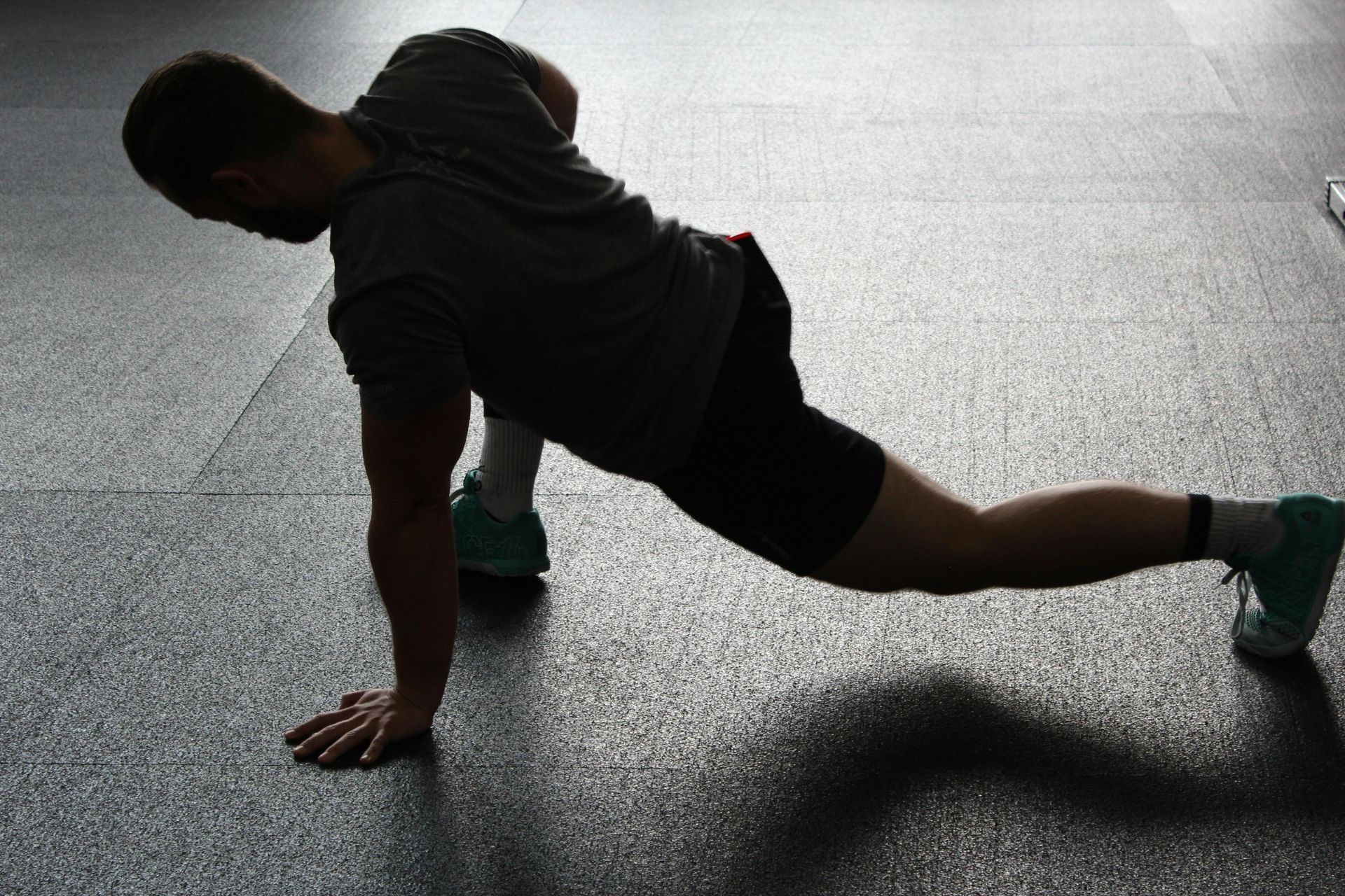 Man performing a lunge stretch on a dark floor. He's wearing a gray shirt and shorts, twisting his torso.