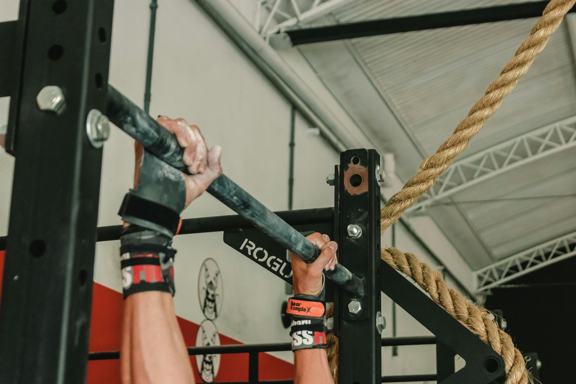 Person gripping a pull-up bar, with wrist straps, in a gym.