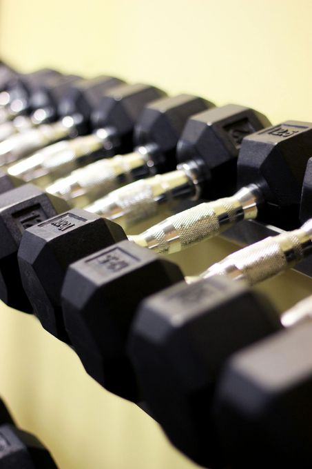 Row of black dumbbells on a rack, metal handles, set against a light yellow wall.