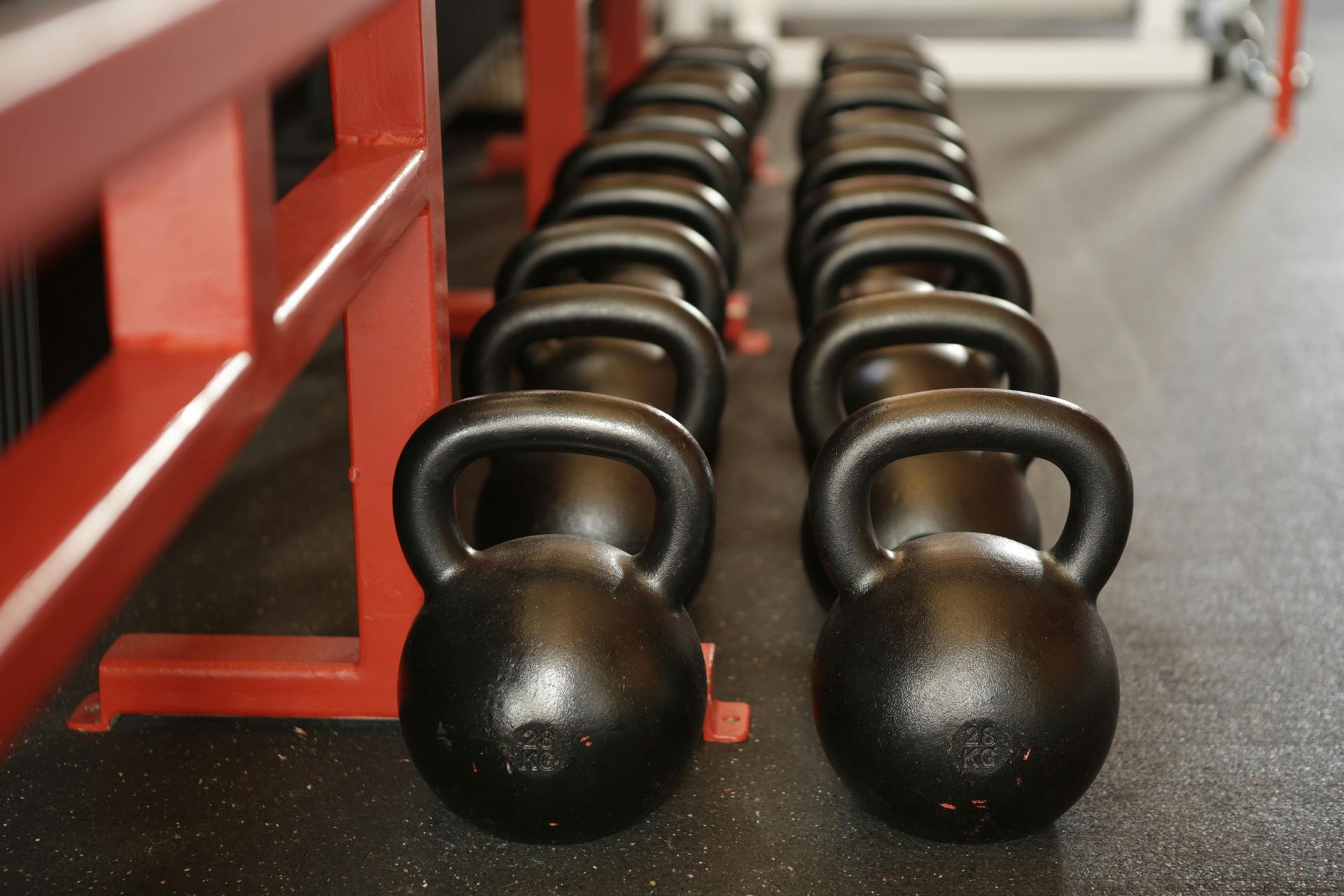 Black kettlebells lined up on the floor of a gym, ready for use.
