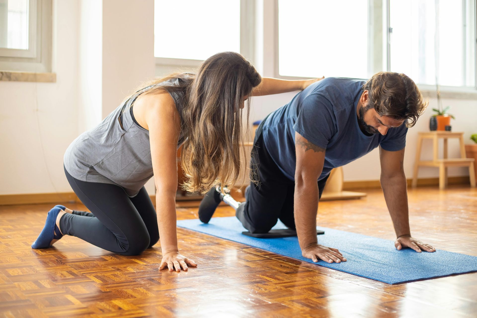 Woman assists man in push-up on mat in a room, likely for physical therapy.