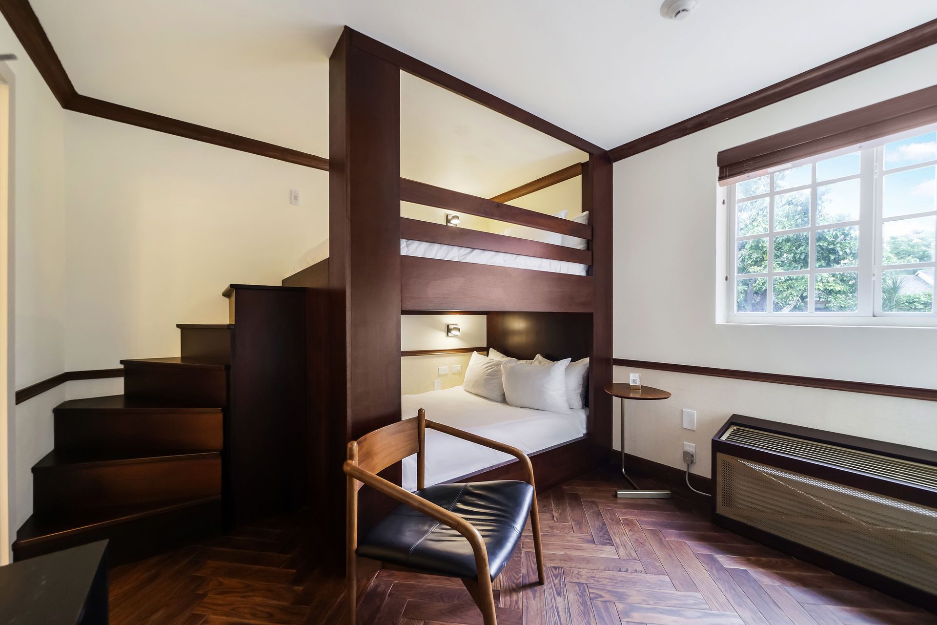 A small hotel room with a bunk bed setup. Staircase leads to the top bunk. Wooden floors and trim.