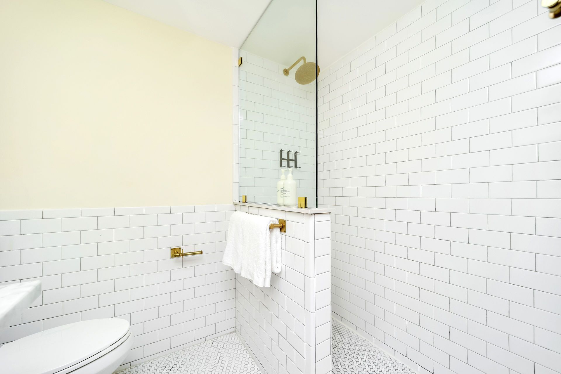 White-tiled bathroom with shower, gold fixtures, and a glass shower door.